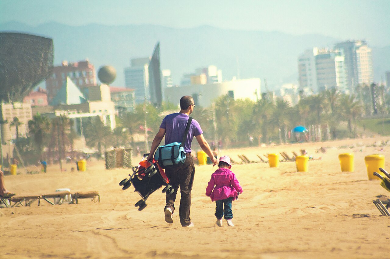 Pessoas a caminhar na areia da Barceloneta, com a cidade ao fundo