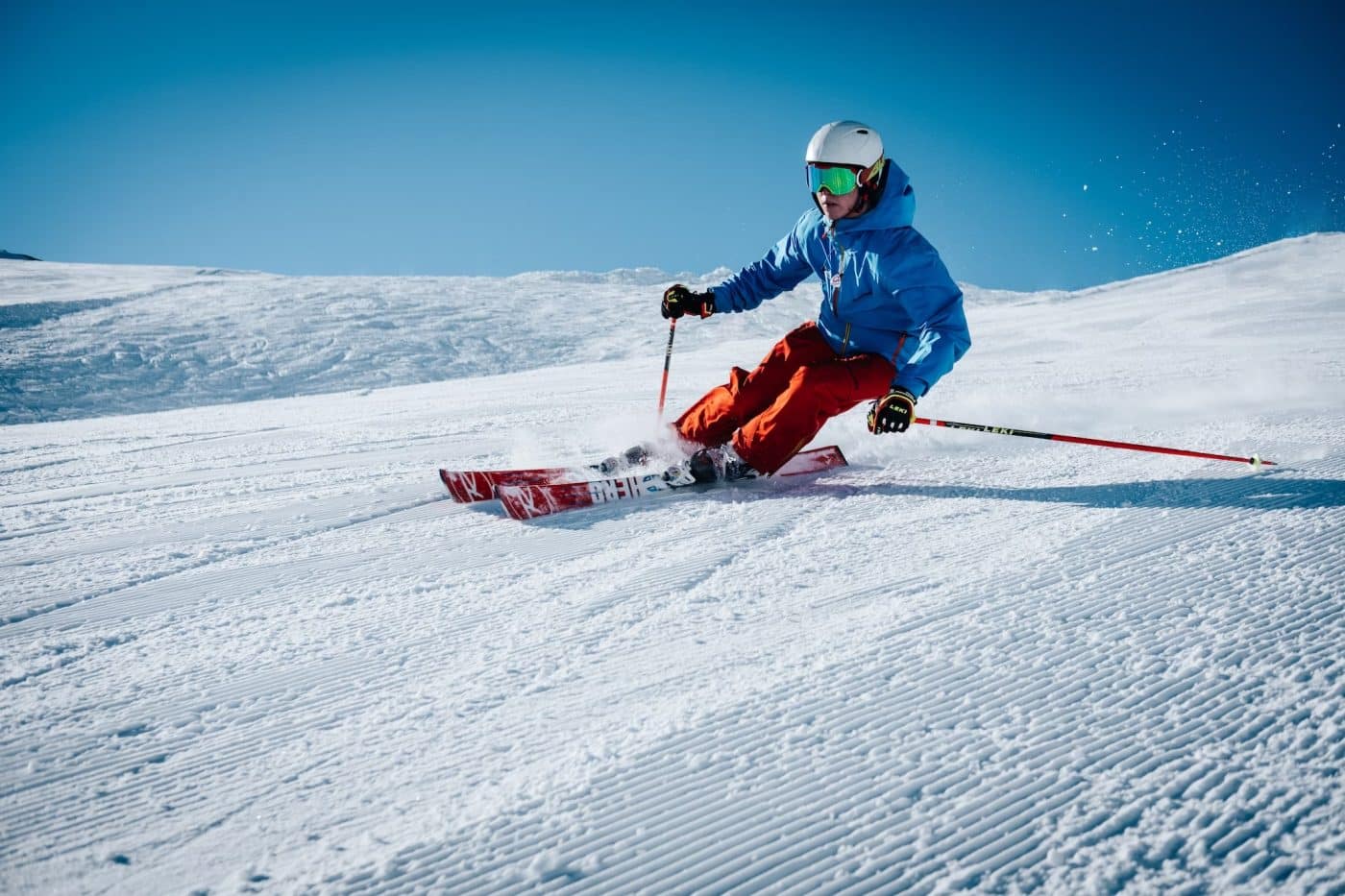 Esquiador com capacete e bastões a descer uma pista nevada